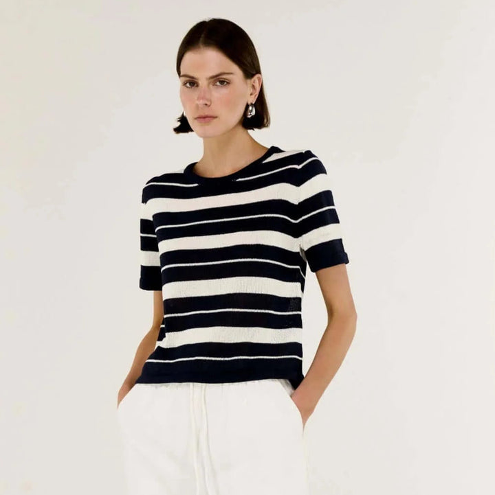 Woman wearing a black and white striped shirt with white pants on a plain background