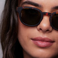 Close-up of a person wearing tortoiseshell sunglasses with a neutral background