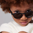 Child wearing black sunglasses with a neutral background