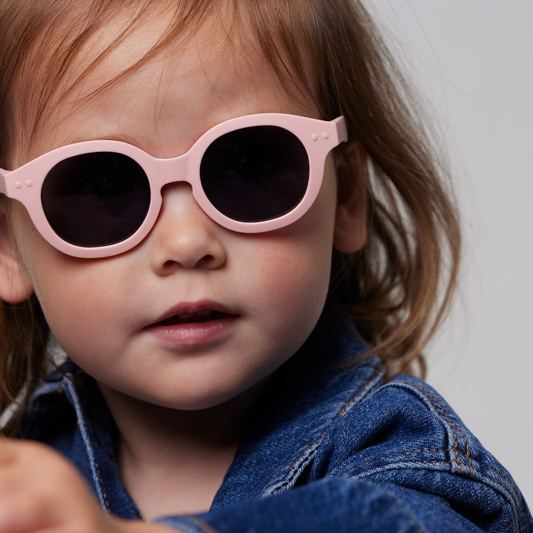 Child wearing pink sunglasses with a neutral background