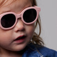 Child wearing pink sunglasses with a neutral background