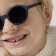 Close-up of a child wearing blue sunglasses with a neutral background