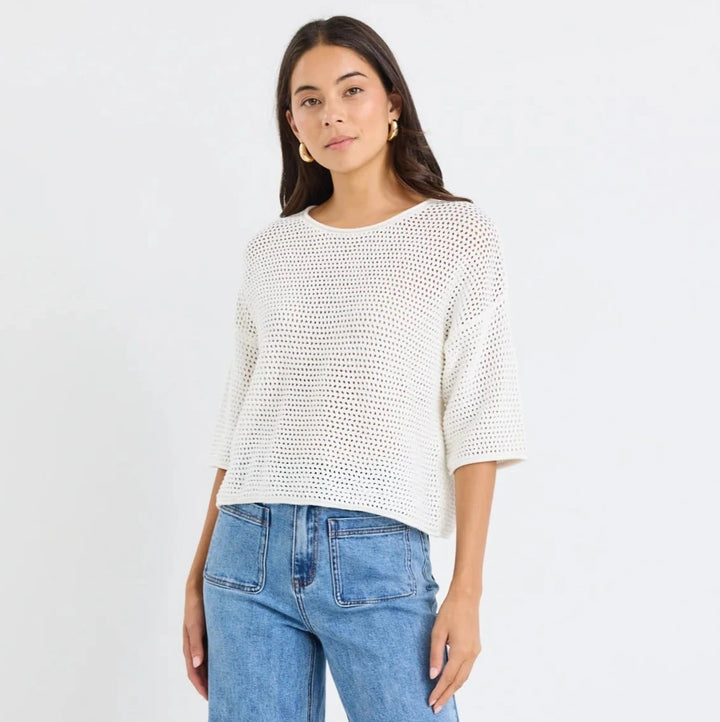 Woman wearing a white textured top and blue jeans on a white background