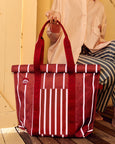 Red and white striped tote bag held by a person against a yellow wall.