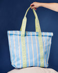 Blue and yellow striped tote bag with text held by a hand against a blue background