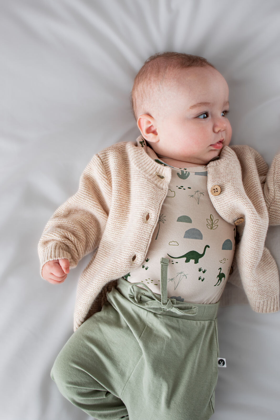 Baby wearing a beige cardigan, green pants, and a graphic t-shirt on a light gray background