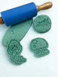 Green play dough with stampers and a rolling pin on a white background