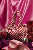 Red and white checkered handbag with pink and red shoes on a pink fabric background