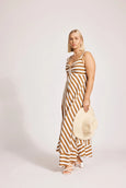 Woman wearing a eb and ive striped dress holding a hat against a plain background