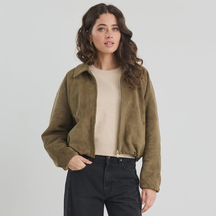 Woman wearing a green jacket, beige shirt, black pants, and white sneakers on a white background