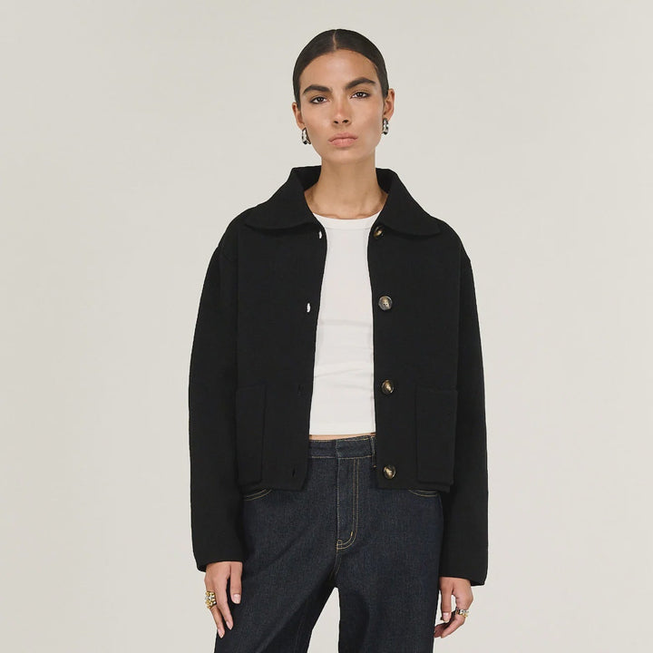 Woman wearing a black coat, white shirt, and dark jeans on a white background