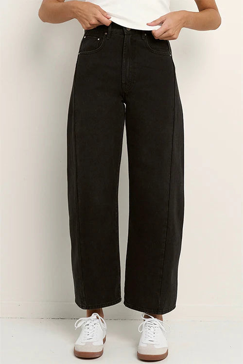 Person wearing black wide-leg jeans and white sneakers on a plain background
