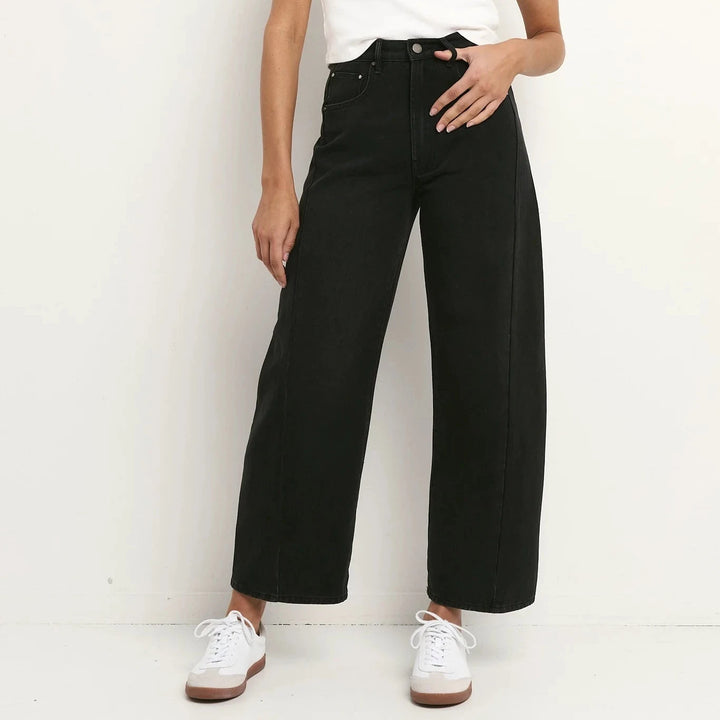 Woman wearing a white sleeveless top and black high-waisted jeans against a white background