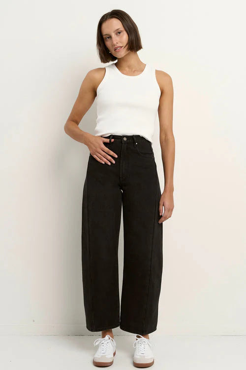Woman wearing a white sleeveless top and black wide-leg jeans against a plain background