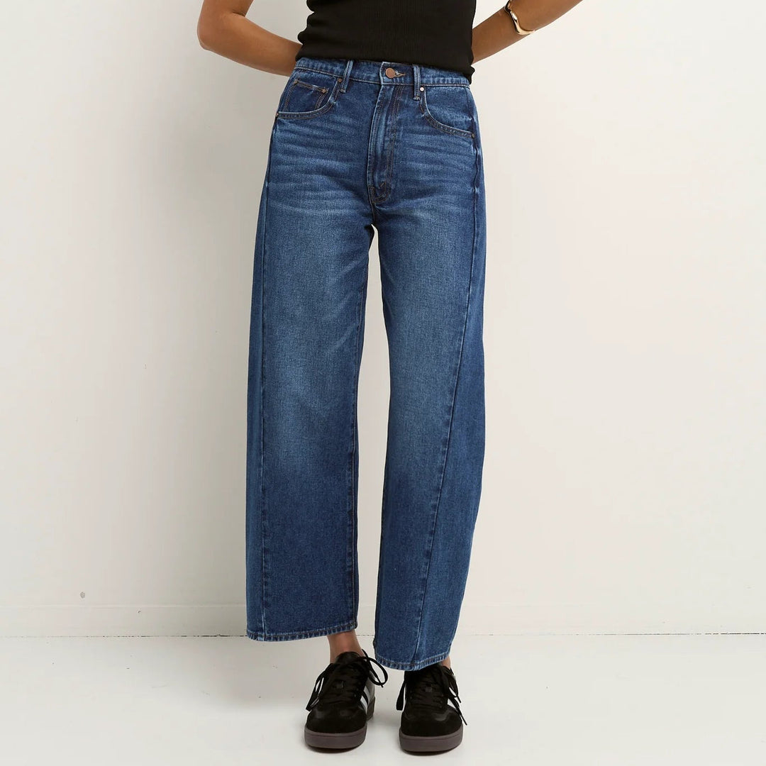 Woman wearing a black tank top and blue Among the brave barrel jeans against a white background