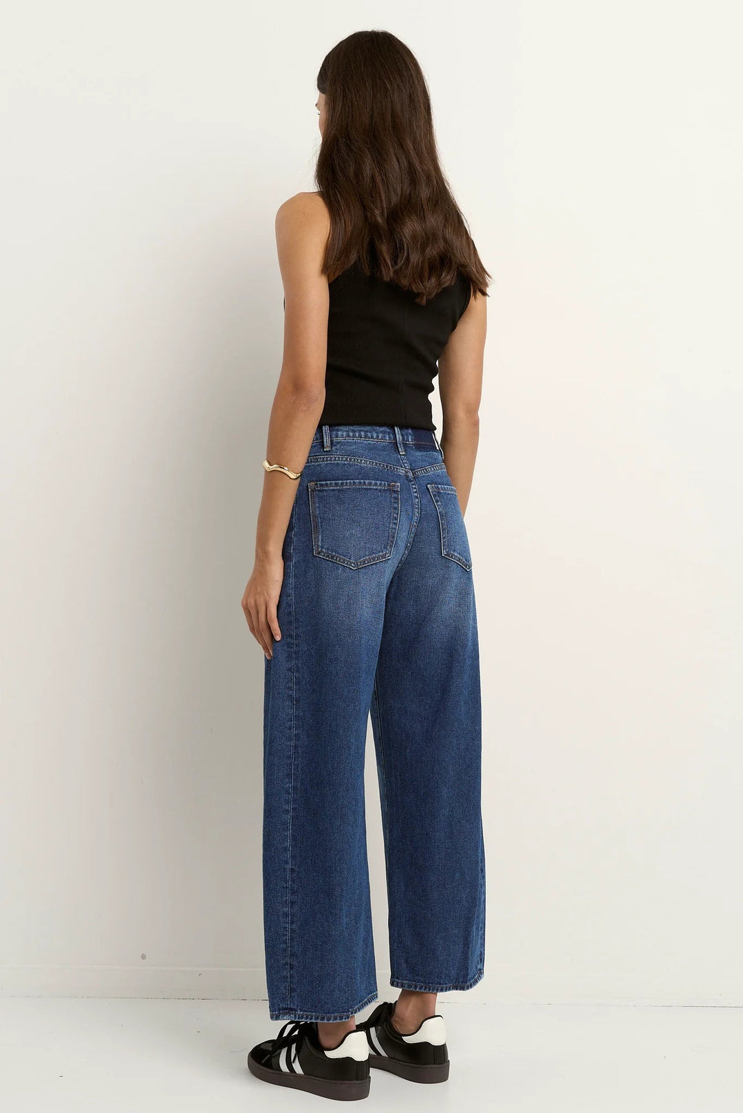 Person wearing blue among the brave barrel jeans and a black top on a white background