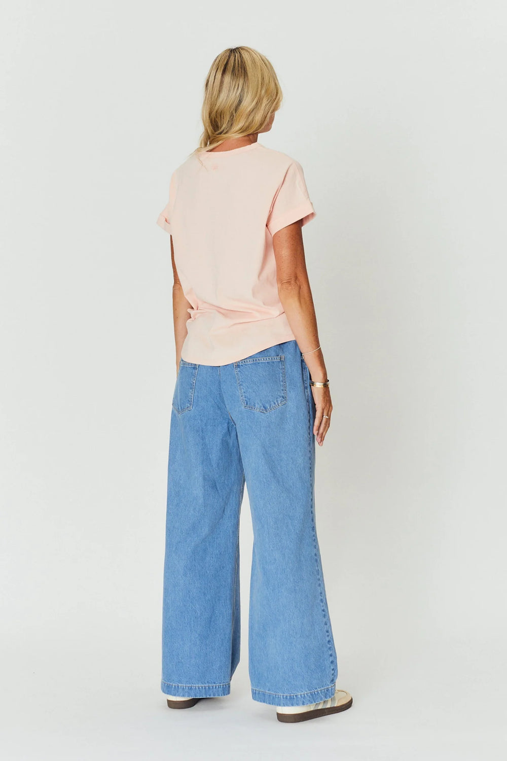 Woman wearing a light pink top and blue jeans on a white background