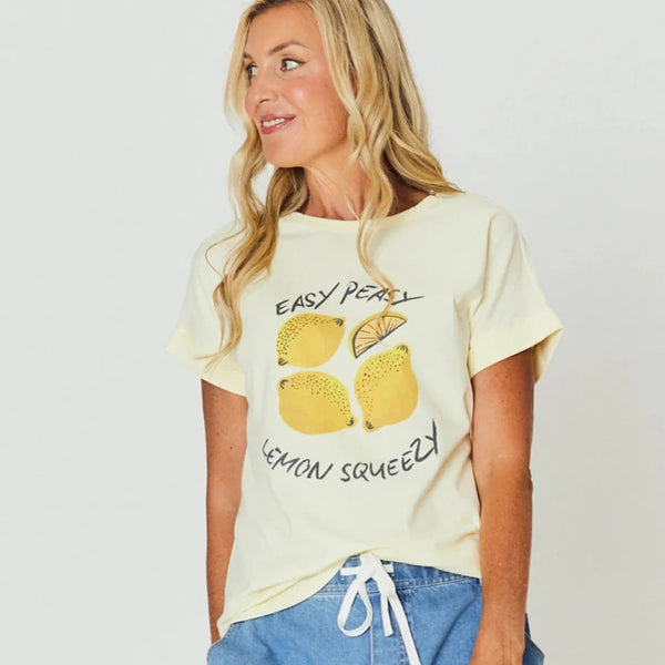 Woman wearing a light yellow t-shirt with lemon graphics and text, standing against a plain background.