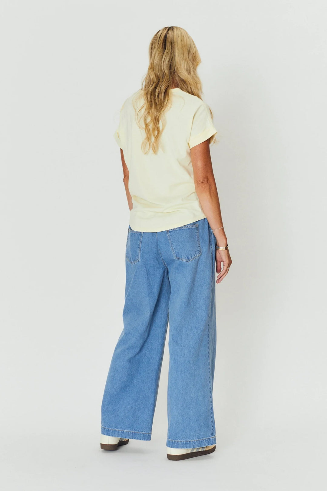 Person wearing a light yellow top and blue jeans on a white background