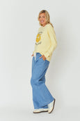 Woman wearing a yellow sweatshirt with a graphic design and blue jeans on a white background