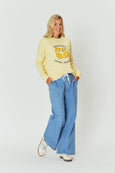 Woman wearing a yellow sweatshirt with a lemon design and blue jeans on a white background