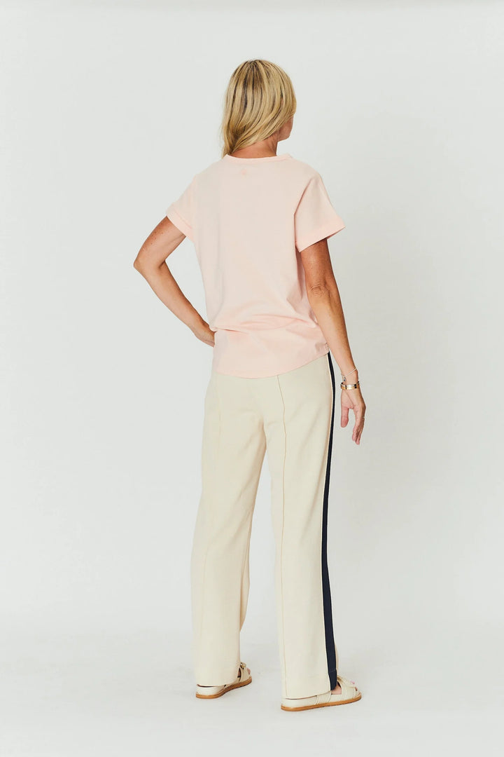 Woman wearing a light pink top and beige pants with a black stripe on a white background
