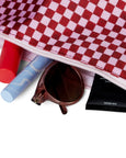 Red and white checkered bag with a blue tube, red item, sunglasses, and black pouch on a white background
