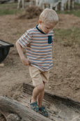 Young boy in a striped shirt standing on a log outdoors