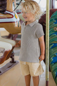 Child in a checkered shirt and shorts standing near a carousel.