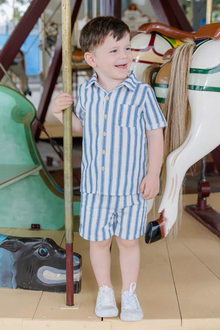 Child in a striped outfit standing next to a carousel horse