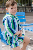 Child wearing a striped poncho sitting on a blue bench.