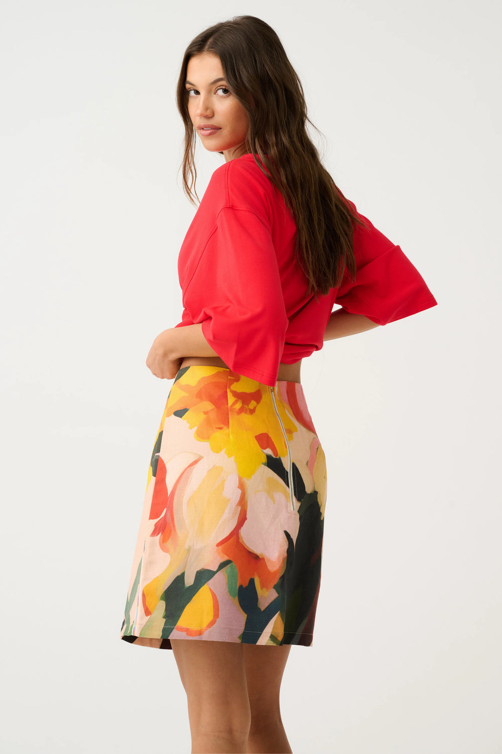Woman wearing a red top and colorful floral skirt on a white background