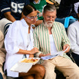 Two people sitting together, one holding a box of food and a menu, in a casual setting.