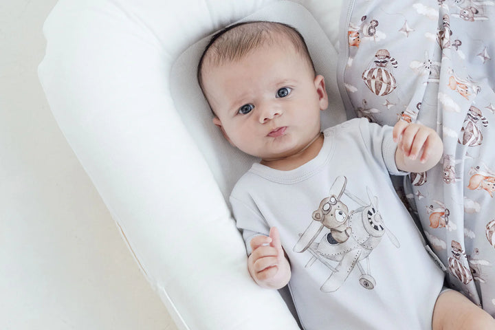 Baby lying on a white cushion with a soft toy in the background