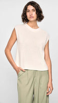 Woman wearing a beige sleeveless top and green pants against a white background