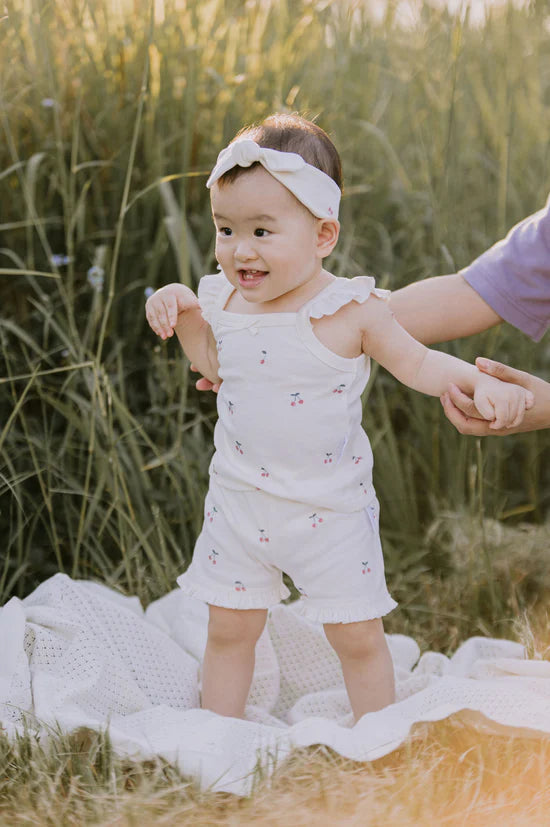 Baby in a white outfit standing in a grassy field with a blurred background