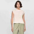 Woman wearing a beige sleeveless top and green pants on a white background