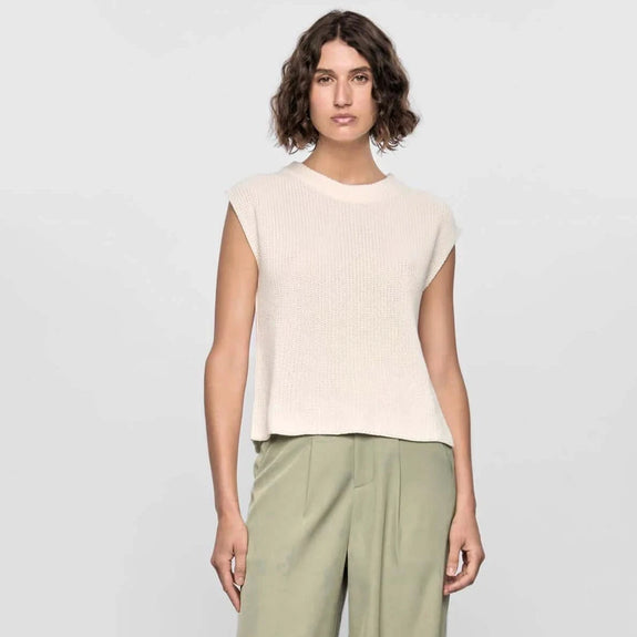 Woman wearing a beige sleeveless top and green pants on a white background