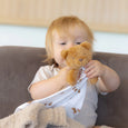 Child holding a teddy bear in a sling on a couch