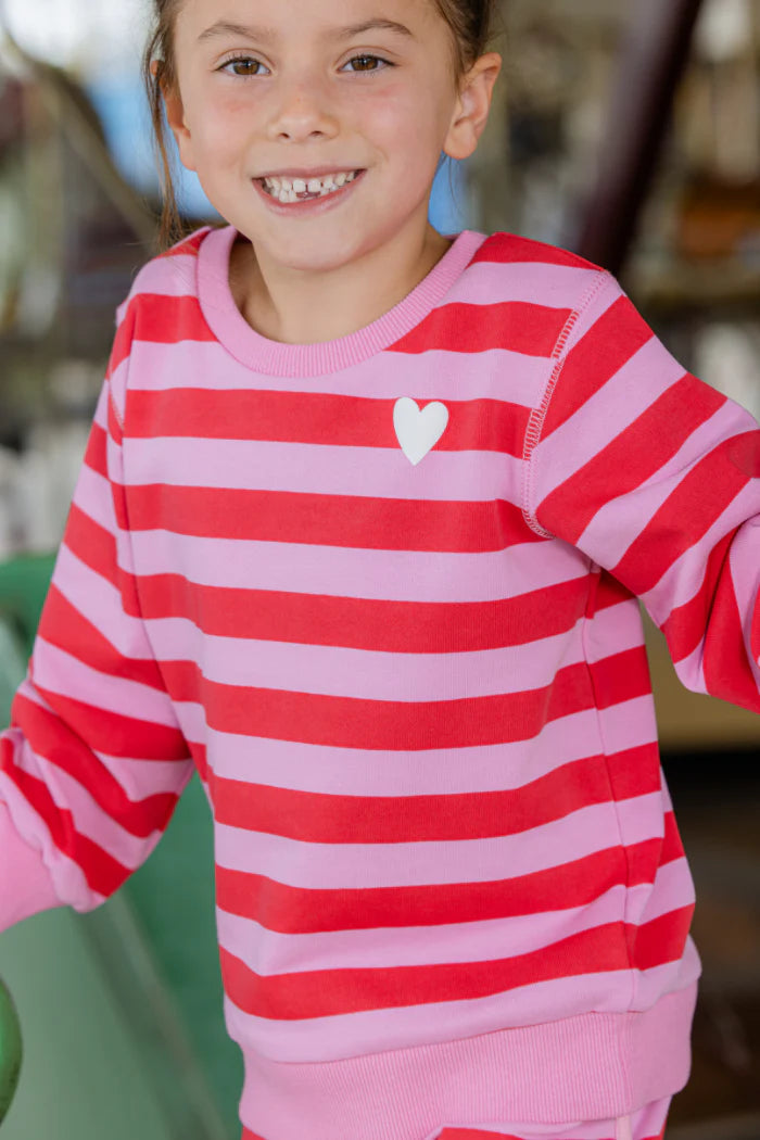 Child wearing a red and pink striped shirt with a heart design.