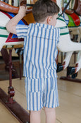 Child in a blue and white striped outfit standing next to a colorful carousel horse.
