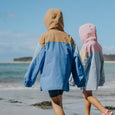 Two people wearing colorful hooded raincoats walking on a beach.