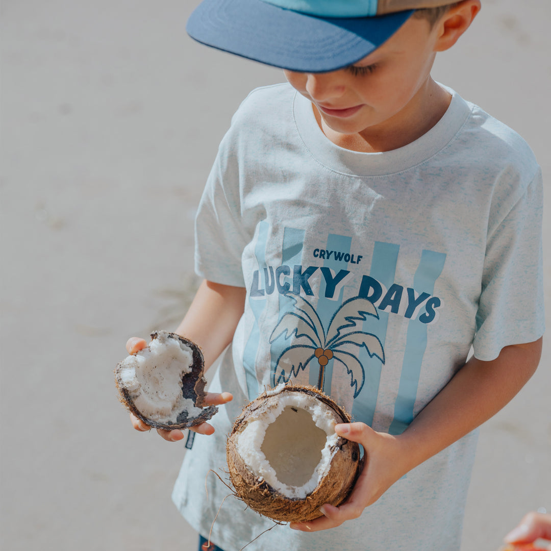 Child holding two coconuts with a crywolf 'Lucky Days' t-shirt in the background