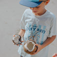 Child holding two coconuts with a crywolf 'Lucky Days' t-shirt in the background