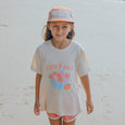 Young girl wearing a 'Lucky Days'CRYWOLF t-shirt and cap on a sandy background