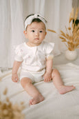 Baby in a white outfit sitting on a soft surface with a neutral background