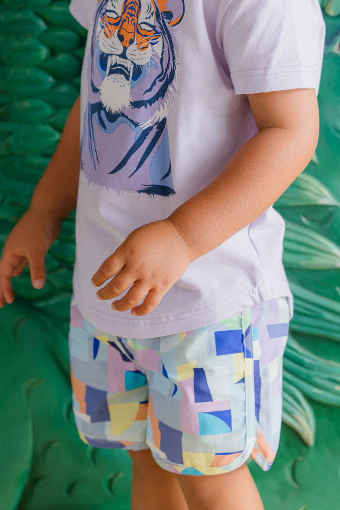 Child wearing a white t-shirt with a tiger design and colorful shorts on a green textured background
