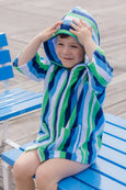 Child wearing a blue, green, and white striped hooded towel sitting on a blue bench.