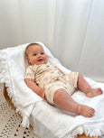 Baby in a lace outfit sitting on a white blanket with a white curtain background