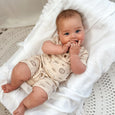 Baby lying on a white textured blanket wearing a beige outfit with animal prints.